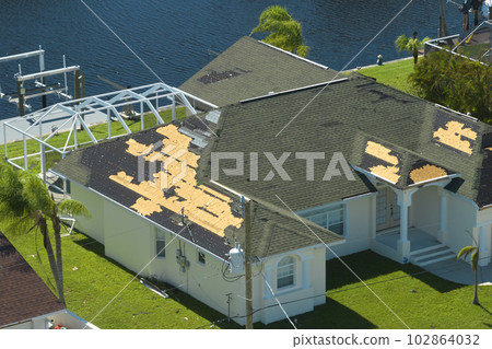 Damaged house roof with missing shingles after hurricane Ian in Florida. Consequences of natural disaster Damaged house roof with missing shingles after hurricane Ian in Florida. Consequences of natural disaster 102864032