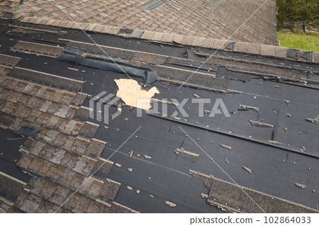 Damaged house roof with missing shingles after hurricane Ian in Florida. Consequences of natural disaster Damaged house roof with missing shingles after hurricane Ian in Florida. Consequences of natural disaster 102864033