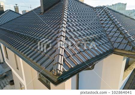Closeup snow guard for safety in winter on house roof top covered with ceramic shingles. Tiled covering of building 102864041