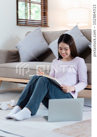 Online education, e-learning. Asian woman in stylish casual clothes, studying using a laptop, listening to online lecture, taking notes, online study at home Online education, e-learning. Asian woman in stylish casual clothes, studying using a laptop, listening to online lecture, taking notes, online study at home 102864313