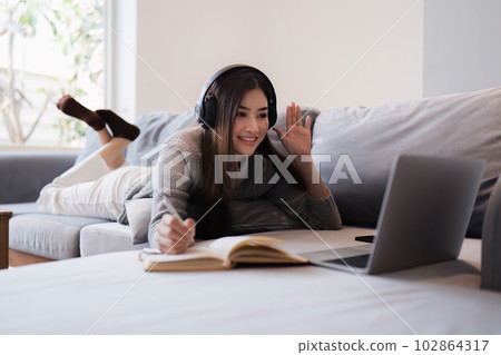 Online education, e-learning. Asian woman in stylish casual clothes, studying using a laptop, listening to online lecture, taking notes, online study at home 102864317