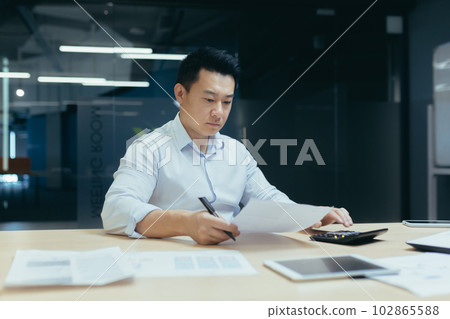 Worried and serious young Asian businessman working in office with documents, busy with paper work, checking accounts on calculator. Worried and serious young Asian businessman working in office with documents, busy with paper work, checking accounts on calculator. 102865588