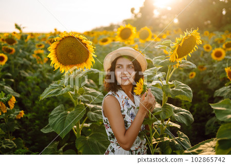 Beautiful woman posing in a field of sunflowers in a dress and hat. Fashion, lifestyle concept. Beautiful woman posing in a field of sunflowers in a dress and hat. Fashion, lifestyle concept. 102865742