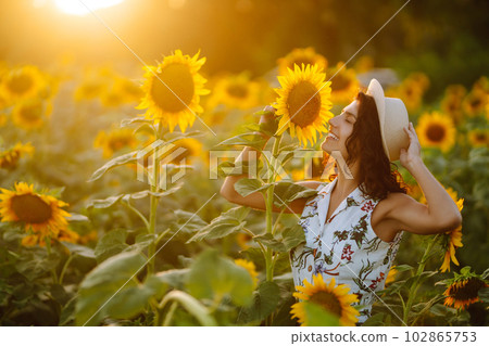 Beautiful woman posing in a field of sunflowers in a dress and hat. Fashion, lifestyle concept. Beautiful woman posing in a field of sunflowers in a dress and hat. Fashion, lifestyle concept. 102865753