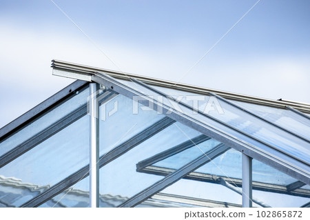 Greenhouse made of glass and metal framing is under bright blue sky Greenhouse made of glass and metal framing is under bright blue sky 102865872