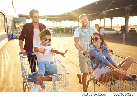 Group of happy young people having fun on shopping trolleys. Multiethnic young people racing on shopping cart. Group of happy young people having fun on shopping trolleys. Multiethnic young people racing on shopping cart. 102866823