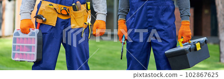 Cropped shot of two male builders in blue overalls carrying toolbox at construction site 102867625
