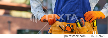 Male builder in blue overalls wearing tool belt. Close up on waist area 102867626