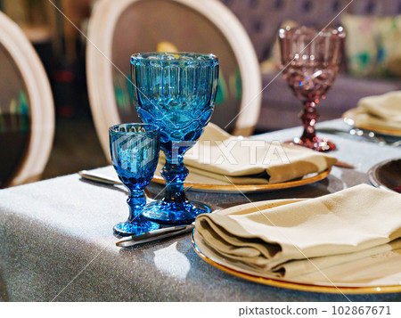 glasses of colored glass on a table with a blue tablecloth. glasses of colored glass on a table with a blue tablecloth. 102867671