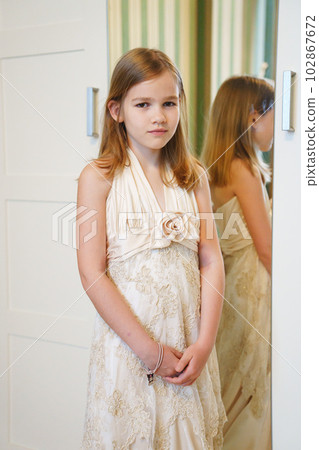 Cute little blonde teenage girl in her mother's wedding dress by the mirror. Cute little blonde teenage girl in her mother's wedding dress by the mirror. 102867672