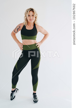 an attractive blonde in a black and green tracksuit poses on a white background. 102867682