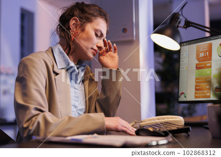 Tired executive manager working overtime at company strategy in startup office, analyzing marketing graphs on computer. Exhausted businesswoman developing investment plan to increase profit 102868312