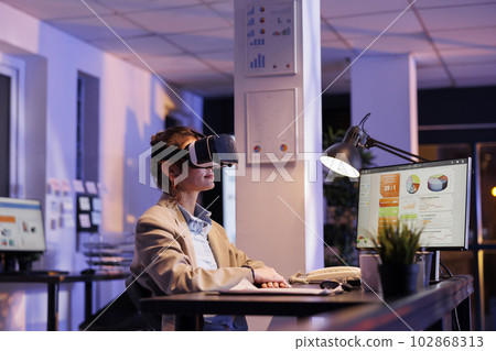 Corporate employeee wearing virtual reality goggles in startup office, analyzing financial growth report. Executive manager working overhours at company strategy using vr headset. Technology concept 102868313