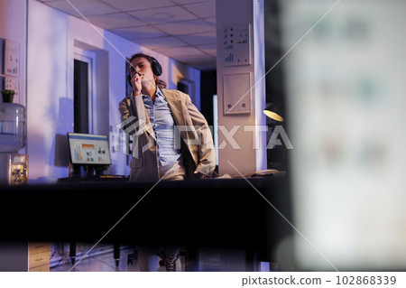 Playful corporate employee singing song at pen, having fun in startup office during work break. Cheerful manager in formal suit working late at night at marketing report, enjoying dancing Playful corporate employee singing song at pen, having fun in startup office during work break. Cheerful manager in formal suit working late at night at marketing report, enjoying dancing 102868339