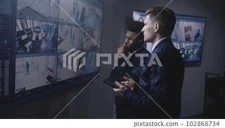 Officer monitors cameras and talks with colleague Officer monitors cameras and talks with colleague 102868734