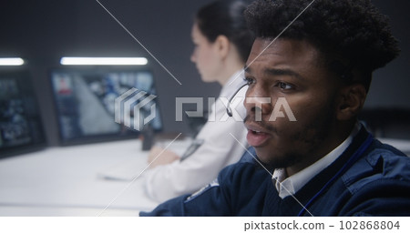 Security operator talks with colleague and types keyboard 102868804