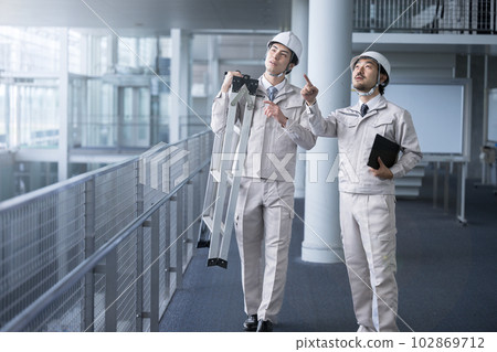 A worker doing inspections and maintenance in a bright warehouse or factory pointing a finger 102869712