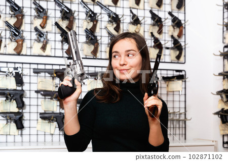 Cheerful woman imitating aiming with two handguns in gun shop Cheerful woman imitating aiming with two handguns in gun shop 102871102