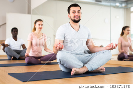 Smiling young man sitting in lotus pose in fitness room Smiling young man sitting in lotus pose in fitness room 102871178