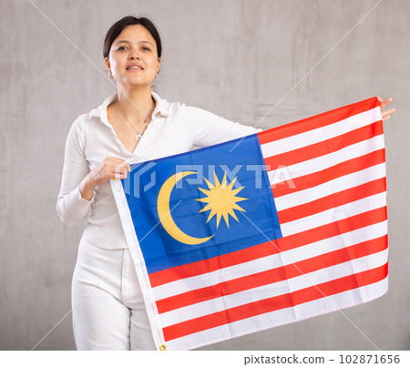 Reliant positive young woman holds big national flag of Malaysia with confident smile showing teeth. Reliant positive young woman holds big national flag of Malaysia with confident smile showing teeth. 102871656