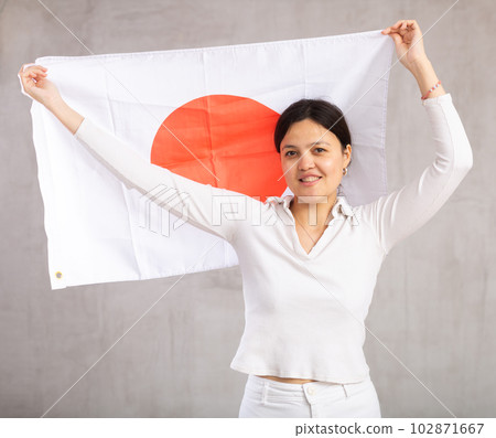 Reliant positive young woman holds big national flag of Japan with confident smile showing teeth 102871667