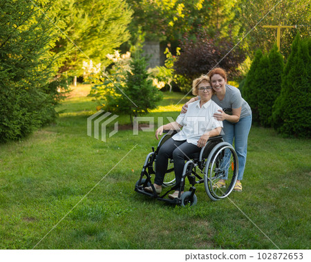 Caucasian woman hugging an elderly mother sitting in a wheelchair. Walk outdoors. Caucasian woman hugging an elderly mother sitting in a wheelchair. Walk outdoors. 102872653