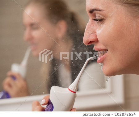 A woman with braces on her teeth uses an irrigator. Close-up portrait.  102872654