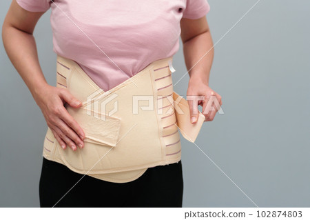 woman wearing lumbar support belts. pregnant and postnatal lumbar brace woman wearing lumbar support belts. pregnant and postnatal lumbar brace 102874803