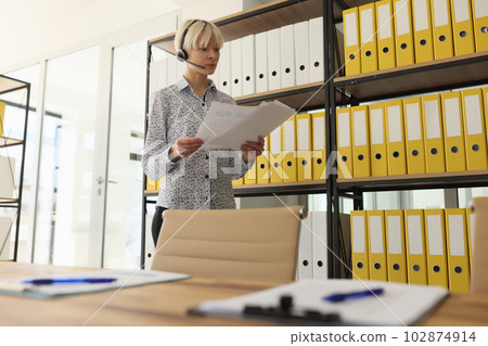 Woman with headset looks at papers in company room at rack Woman with headset looks at papers in company room at rack 102874914