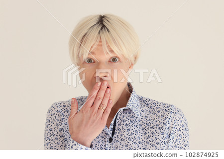 Surprised woman with dyed blonde hair covers mouth with palm 102874925