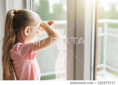 Sad little girl looking through  window at home. 102875517