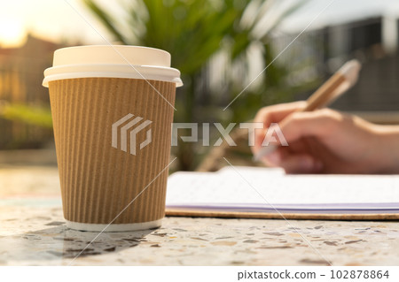 Unrecognizable Young woman study in beach resort. Drinking coffee from paper cup. Student making homework Female hands writing on notebook gratitude journal self reflection self discovery in Co Unrecognizable Young woman study in beach resort. Drinking coffee from paper cup. Student making homework Female hands writing on notebook gratitude journal self reflection self discovery in Co 102878864