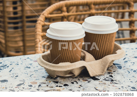 Two paper cups with lid for tea to go. Coffee take away on the table. Take-out coffees with brown paper cup holder. Brown safety cardboard collars. Cardboard tray 102878868