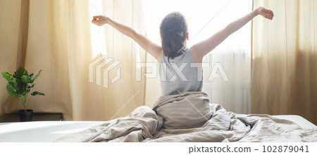 little boy sitting and stretching in bed at home in the morning on a window background 102879041