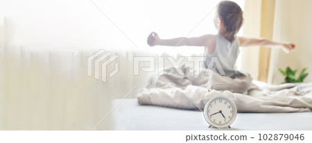 little boy sitting and stretching in bed at home in the morning with alarm clock little boy sitting and stretching in bed at home in the morning with alarm clock 102879046