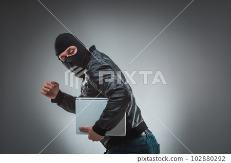Thief stealing a laptop computer. Isolated on gray background 102880292