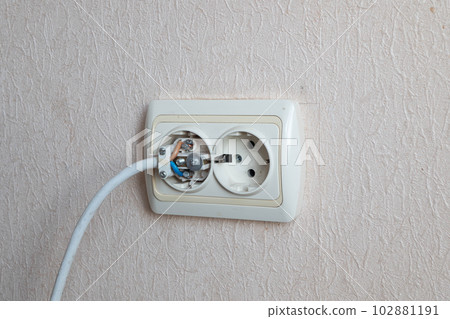 Household electrical outlet with a broken electrical plug inside. Bare live wires sticking out of the Electric socket installed in the wall and connected to the electricity power grid. Wiring Devices Household electrical outlet with a broken electrical plug inside. Bare live wires sticking out of the Electric socket installed in the wall and connected to the electricity power grid. Wiring Devices 102881191