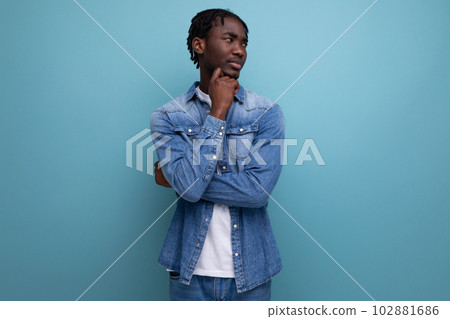 pensive brunette man with dreadlocks in a denim jacket on a blue background 102881686