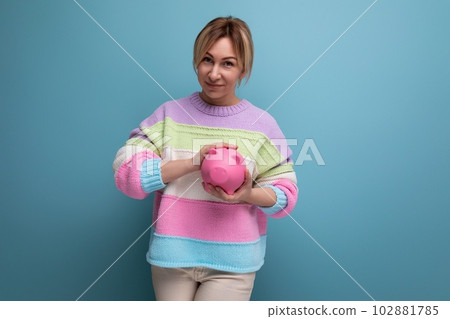 close-up photo of an attractive blond woman in a striped sweater with a piggy bank of coins on a close-up photo of an attractive blond woman in a striped sweater with a piggy bank of coins on a 102881785