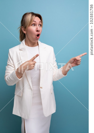 young surprised blondie elegant female adult wearing jacket and dress points finger to the side 102881786