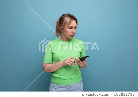 doubtful attractive blond girl holding a smartphone in her hand on a blue background with copy space doubtful attractive blond girl holding a smartphone in her hand on a blue background with copy space 102881792