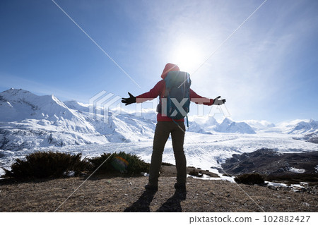 Woman hiker enjoy the view on mountain top cliff edge face to glacier mountains Woman hiker enjoy the view on mountain top cliff edge face to glacier mountains 102882427