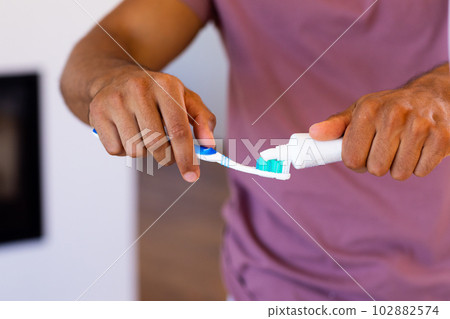 Midsection of biracial man putting toothpaste on toothbrush in bathroom 102882574
