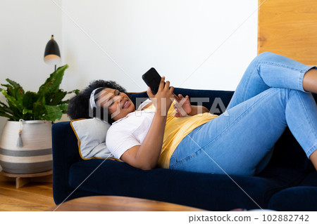 Happy plus size african american woman lying on sofa and using smartphone Happy plus size african american woman lying on sofa and using smartphone 102882742