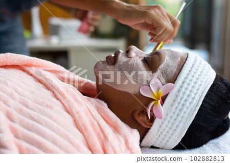 Relaxed plus size african american woman having beauty face mask applied to face at spa 102882813