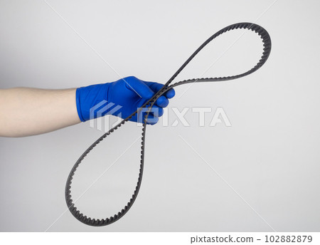Timing belt cracked. Replacing a failed engine transmission belt. Cracks in rubber and risk of broken cords. Replacement of equipment according to the regulations. Mechanic in blue gloves Timing belt cracked. Replacing a failed engine transmission belt. Cracks in rubber and risk of broken cords. Replacement of equipment according to the regulations. Mechanic in blue gloves 102882879