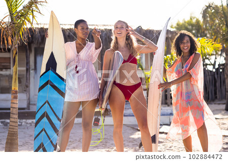 Happy diverse female friends holding surfboards at beach Happy diverse female friends holding surfboards at beach 102884472