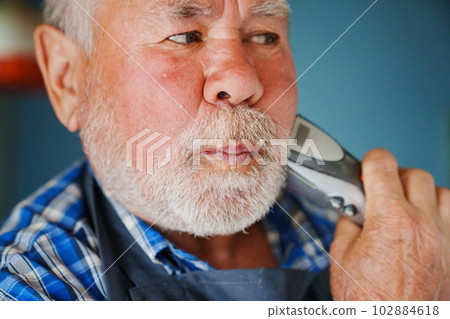 An elderly man trims his beard with an eclectic razor. ease of use of clippers. 102884618