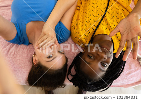 Happy diverse teenager girls friends lying on bed and taking selfie Happy diverse teenager girls friends lying on bed and taking selfie 102884831