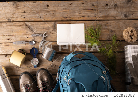 Camping equipment of backpack, metal cup and blank notebook on wooden background with copy space 102885398